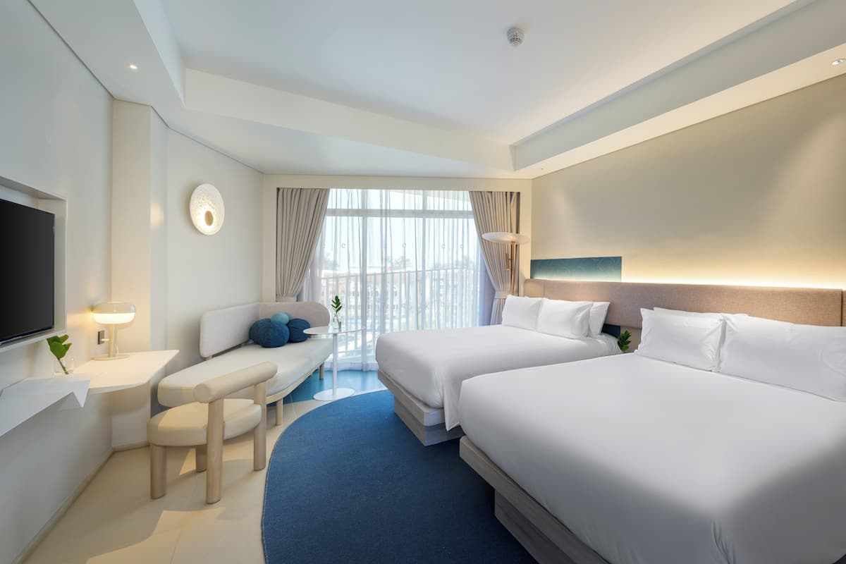A modern hotel room with two beds, a desk, a TV, and a large window with curtains.