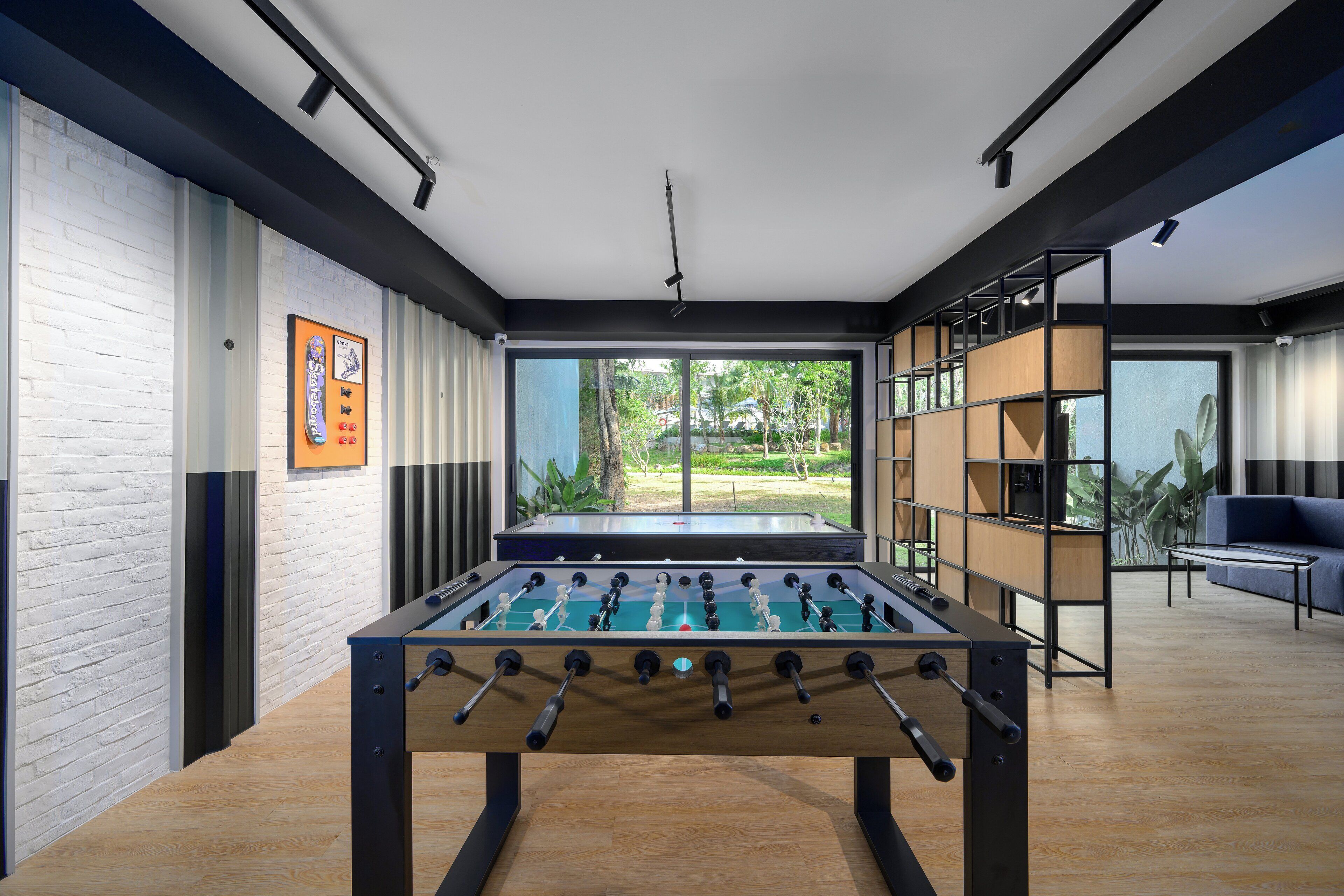 Espaço interior moderno com mesa de futebol, janelas amplas e vista para o verde lá fora.