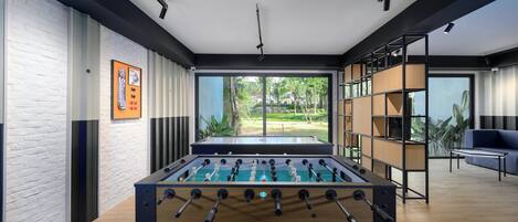 Espaço interior moderno com mesa de futebol, janelas amplas e vista para o verde lá fora.