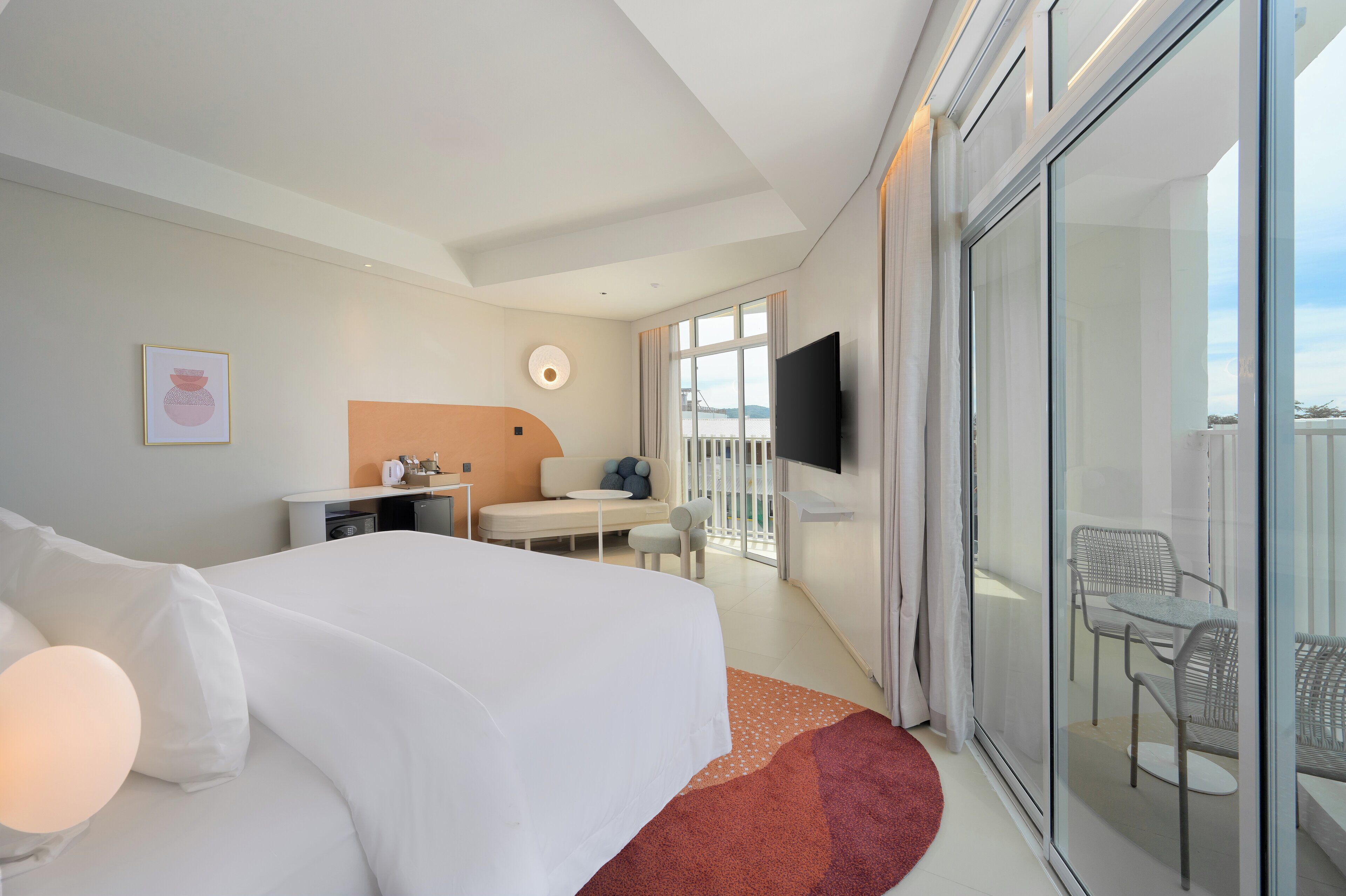 Habitación de hotel con una cama grande, un escritorio con silla, televisión y balcón con mobiliario exterior.