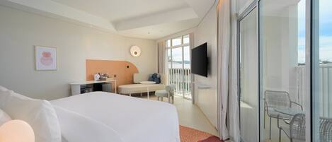 A hotel room with a large bed, a desk with a chair, a TV, and a balcony with outdoor seating.