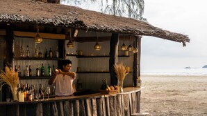 A beachside bar with a rustic wooden structure, shelves with bottles, and hanging lights. - Aana Resort & Spa (Ko Chang)