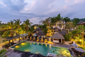 Um resort com piscina, construções de palha e vegetação exuberante.