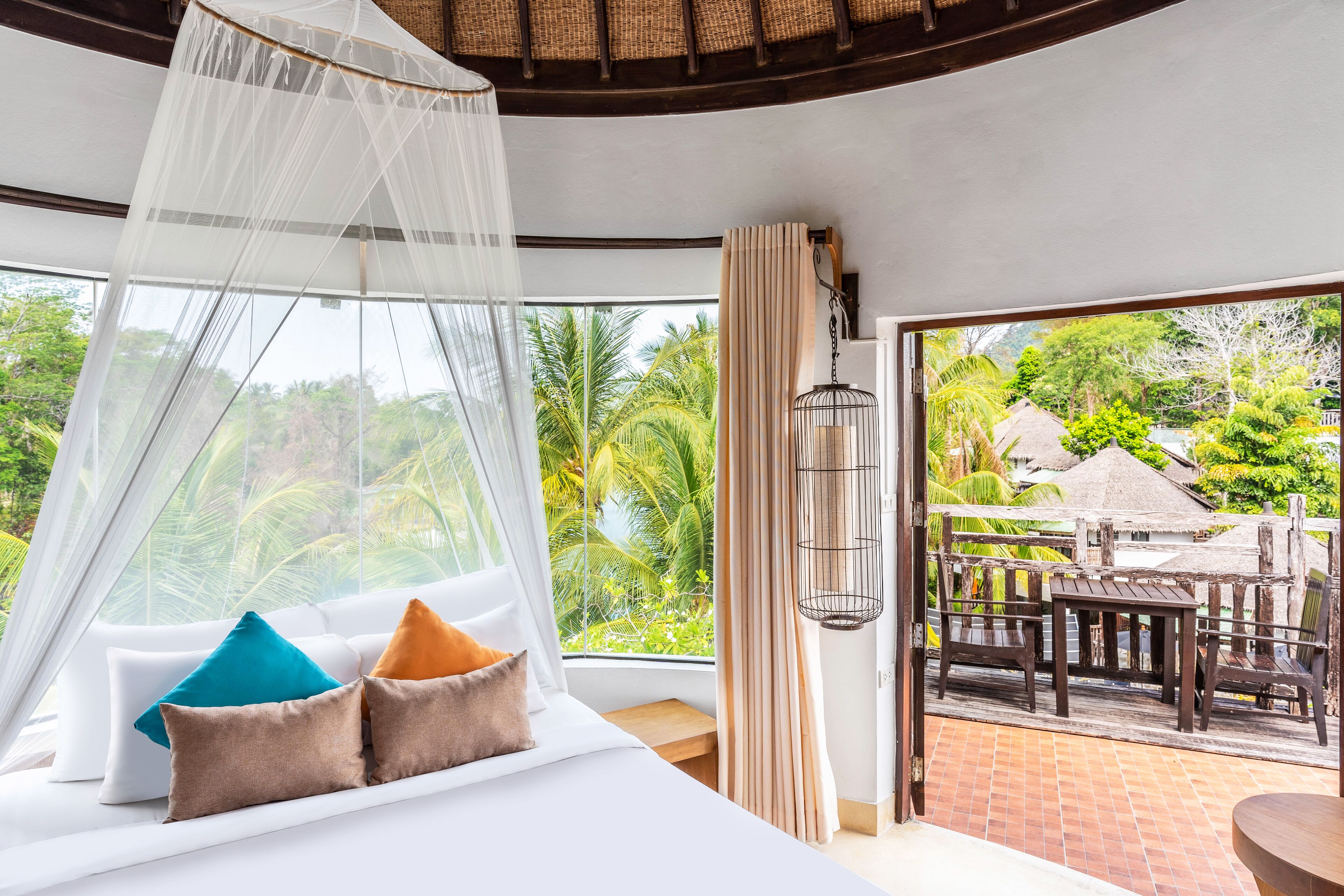 A bedroom with a bed, a window with a view of greenery, and a balcony with outdoor furniture.
