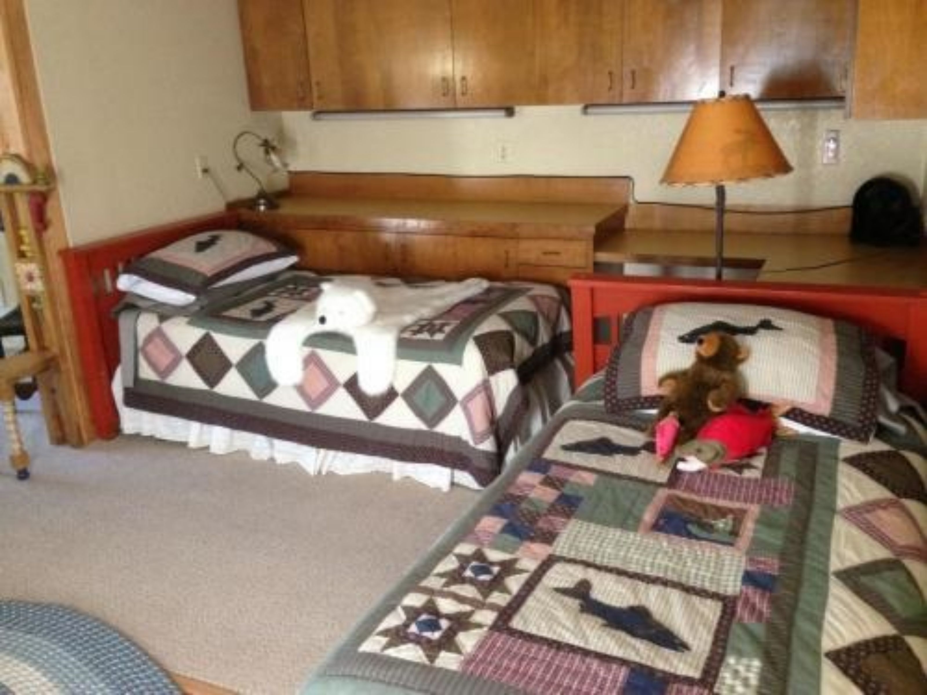 Een slaapkamer met twee bedden, een houten hoofdbord, een nachtkastje, een lamp en een teddybeer op een van de bedden.