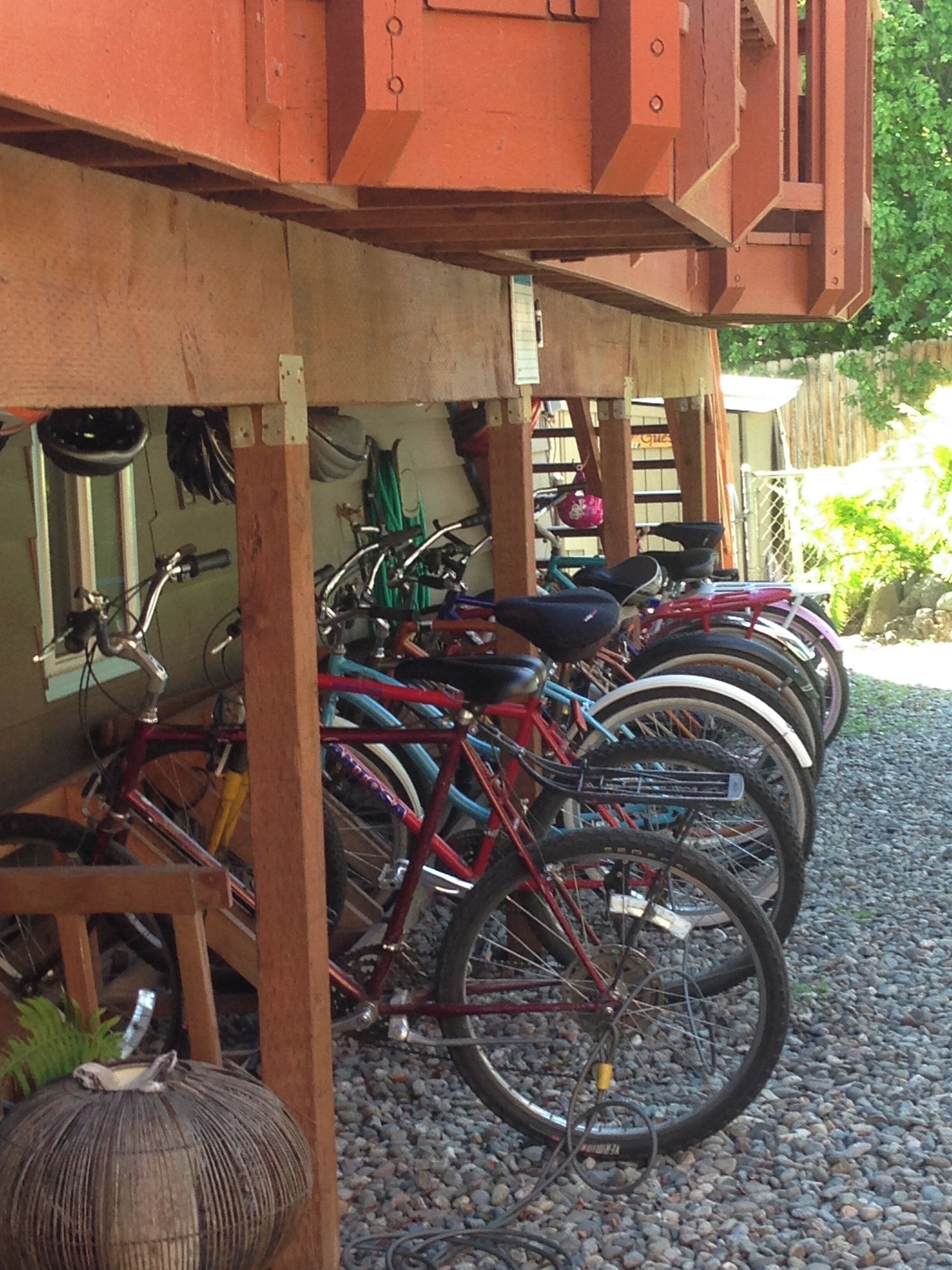 Bicycles parked under a wooden structure with a gravel ground.