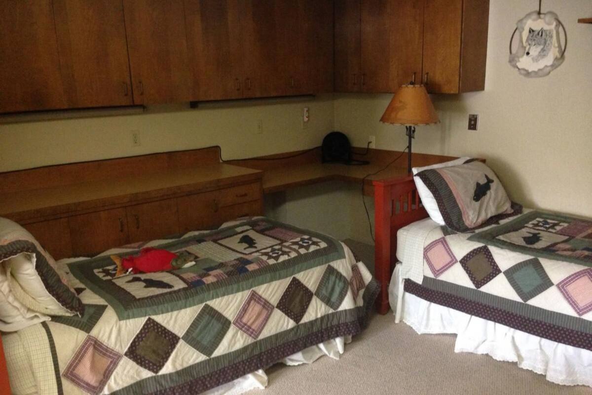 Une chambre avec deux lits simples, une commode en bois, un bureau et une lampe.