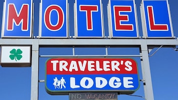 Letrero de motel con el texto 'MOTEL' y 'TRAVELER'S LODGE', un símbolo de trébol de cuatro hojas y un letrero de 'NO VACANCY'.