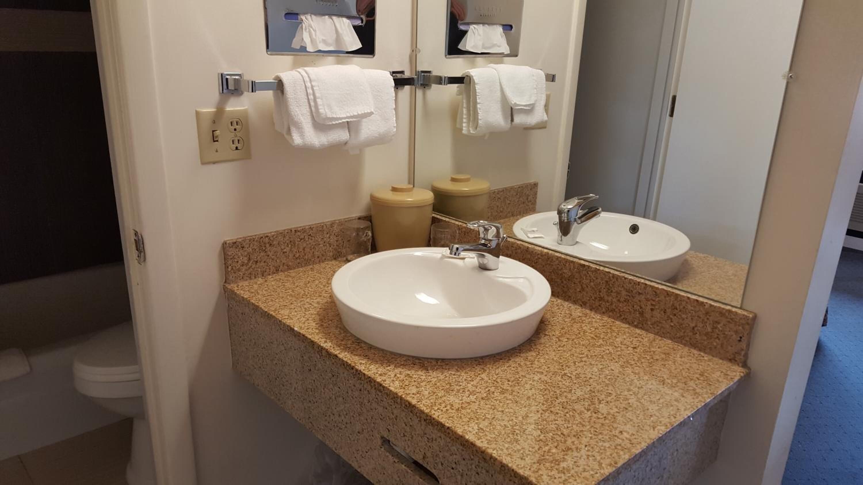 A bathroom with a granite countertop, two sinks, a mirror, and a towel rack.