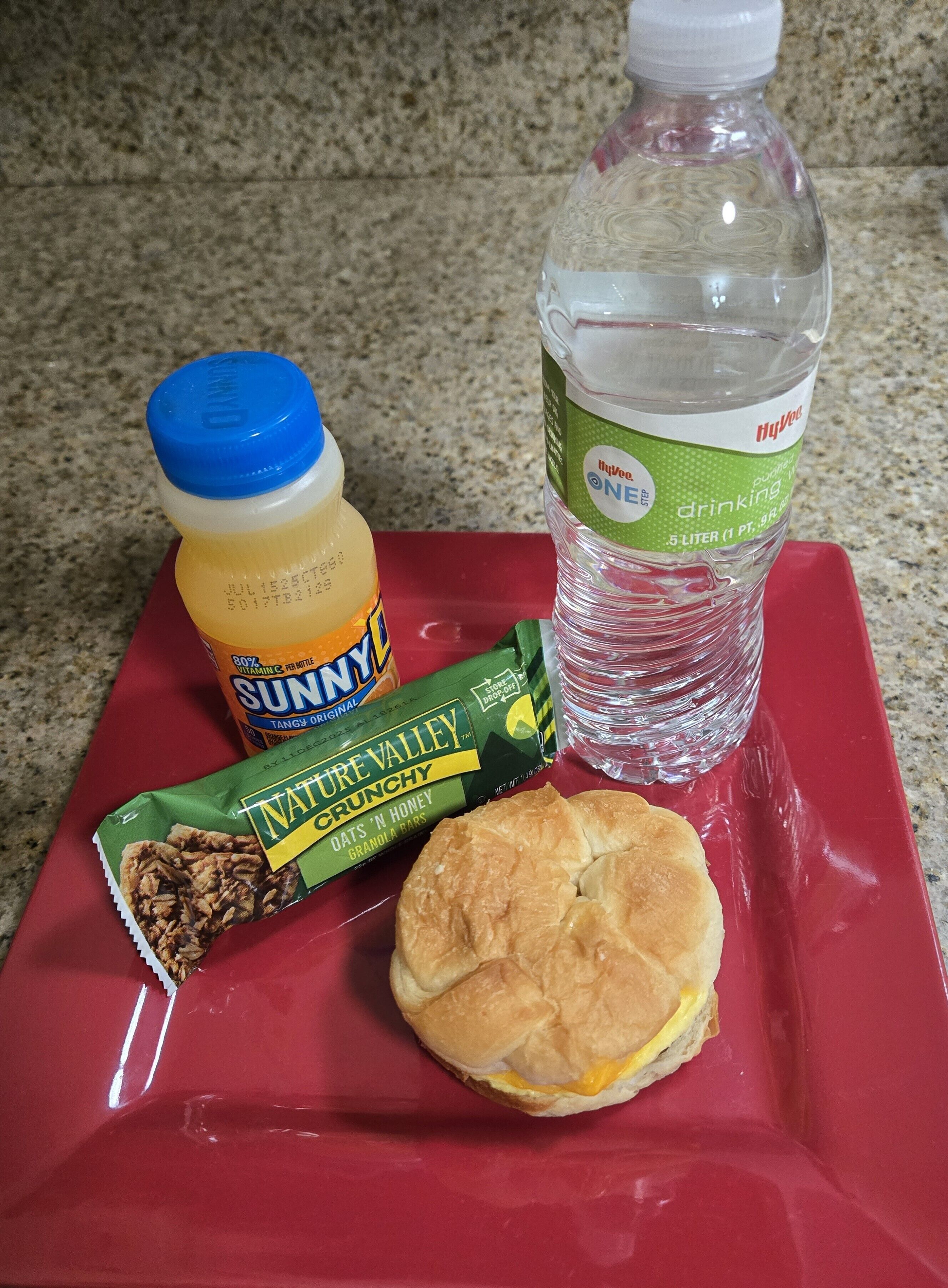 Una bandeja con un sándwich, una botella de jugo y una barra de granola.