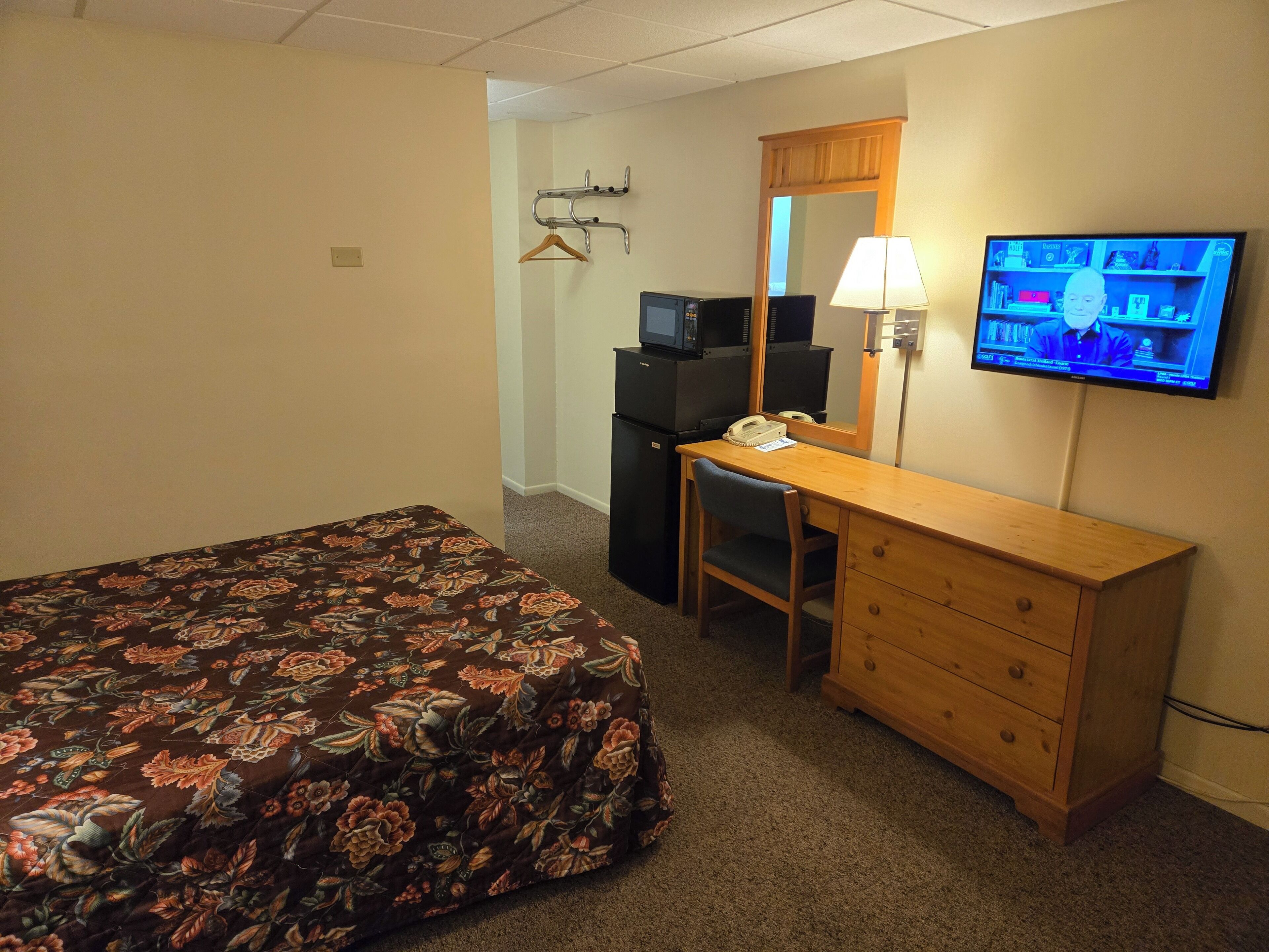 A hotel room with a bed, a desk, a chair, a television, and a mirror.