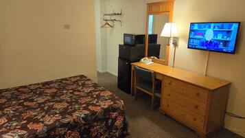 A hotel room with a bed, a desk, a chair, a television, and a mirror.