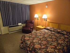 Une chambre d’hôtel équipée d’un lit, d’une chaise, d’un bureau, de deux lampes et d’un appareil de climatisation.