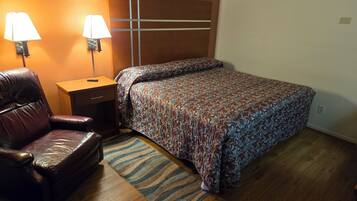 A bedroom with a bed, a leather chair, a nightstand, two wall lamps, and a patterned rug.