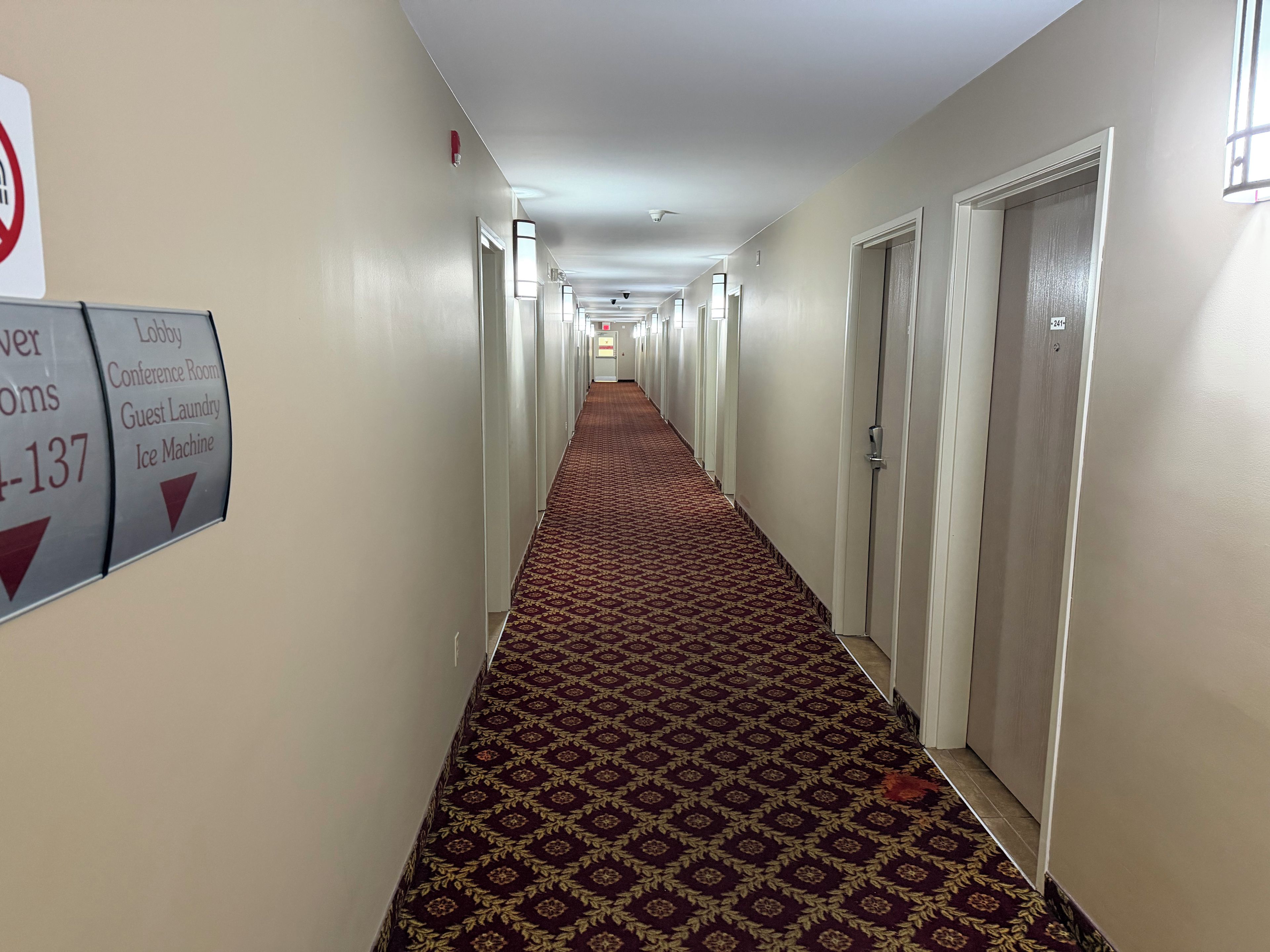 A hotel hallway with a patterned carpet, doors on both sides, and directional signs for amenities like the lobby, conference room, and ice machine.