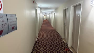 A hotel hallway with a patterned carpet, doors on both sides, and directional signs for amenities like the lobby, conference room, and ice machine.
