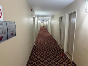Pasillo de hotel con alfombra estampada, puertas a ambos lados y señalización que indica la dirección a servicios como el vestíbulo, la sala de conferencias y la máquina de hielo.