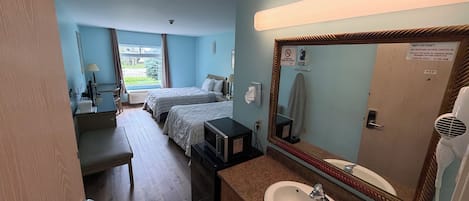A hotel room with two beds, a bathroom with a sink and mirror, and a window with curtains.