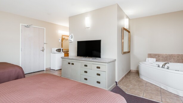 A hotel room with a bed, a TV, a dresser, a bathroom with a bathtub, and a door. - London Travel Inn (London)