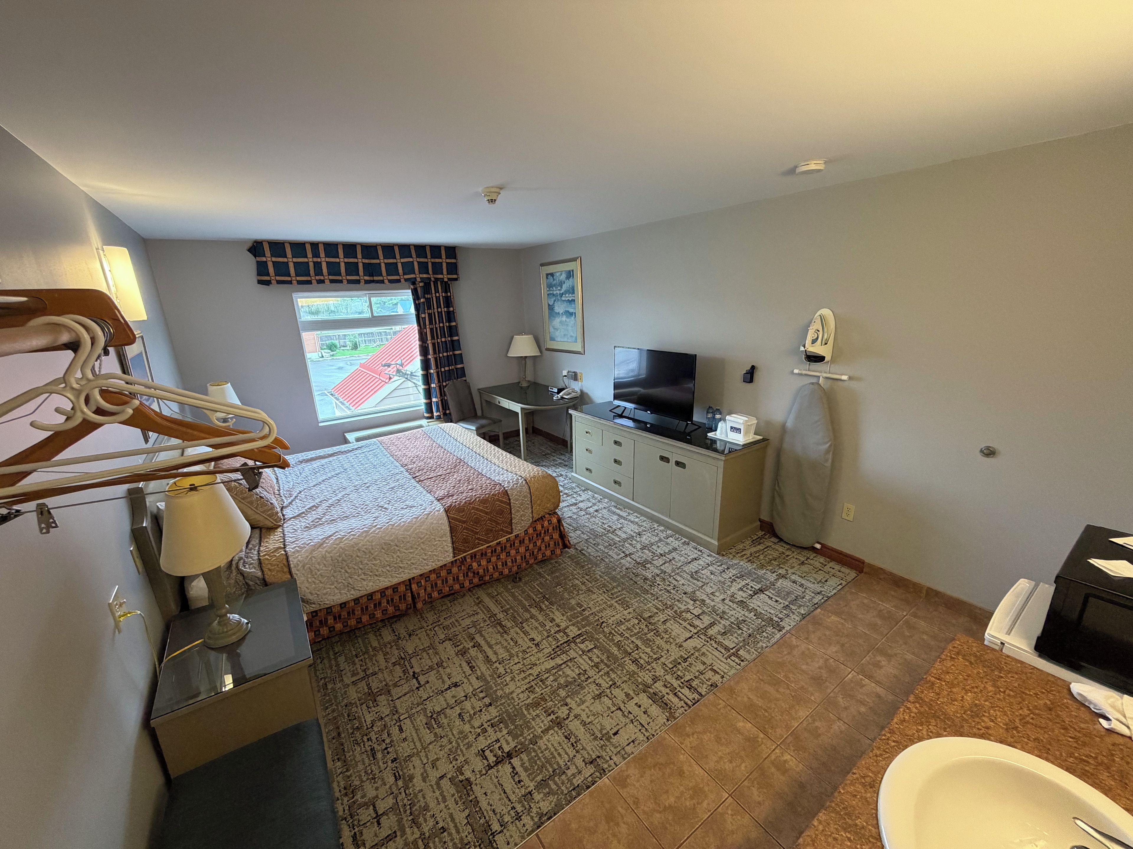 A hotel room with a bed, desk, TV, ironing board, and bathroom.