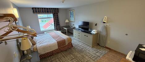 A hotel room with a bed, desk, TV, ironing board, and bathroom.