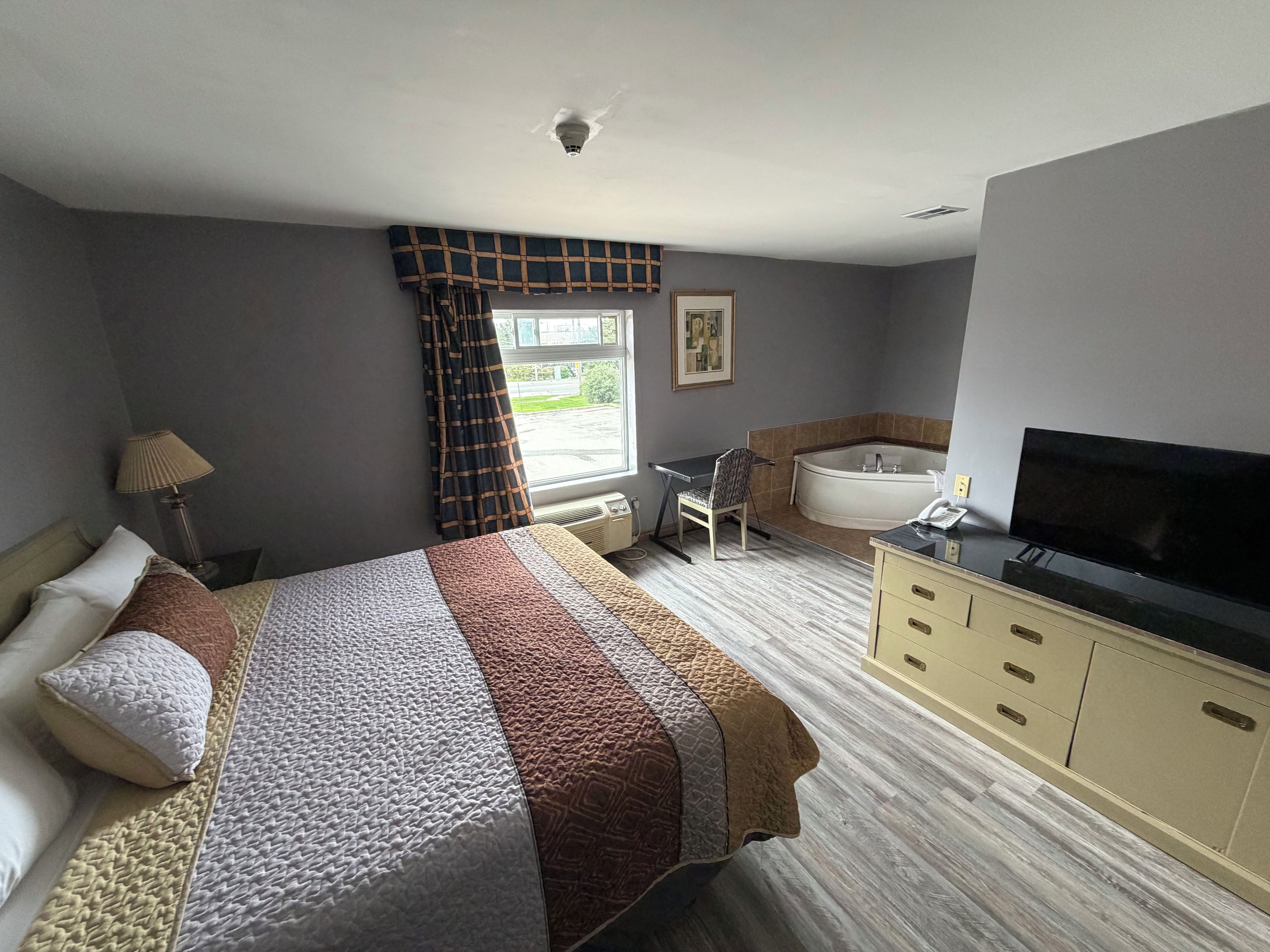 A hotel room with a bed, a desk, a chair, a bathtub, and a television.