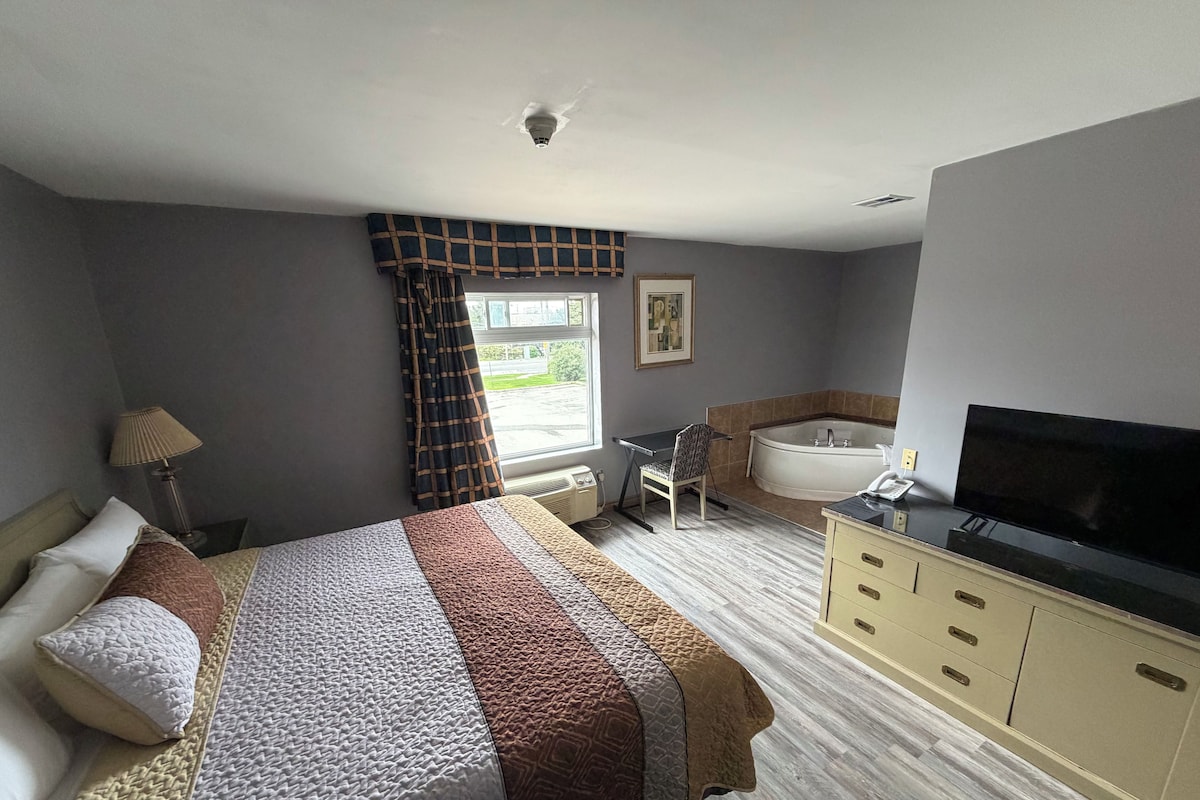 A hotel room with a bed, a desk, a chair, a bathtub, and a television.