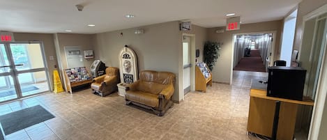 A lobby with a reception desk, two leather armchairs, a plant, and a sign indicating the exit.