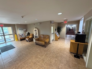 A lobby with a reception desk, two leather armchairs, a plant, and a sign indicating the exit. - London Travel Inn (London)