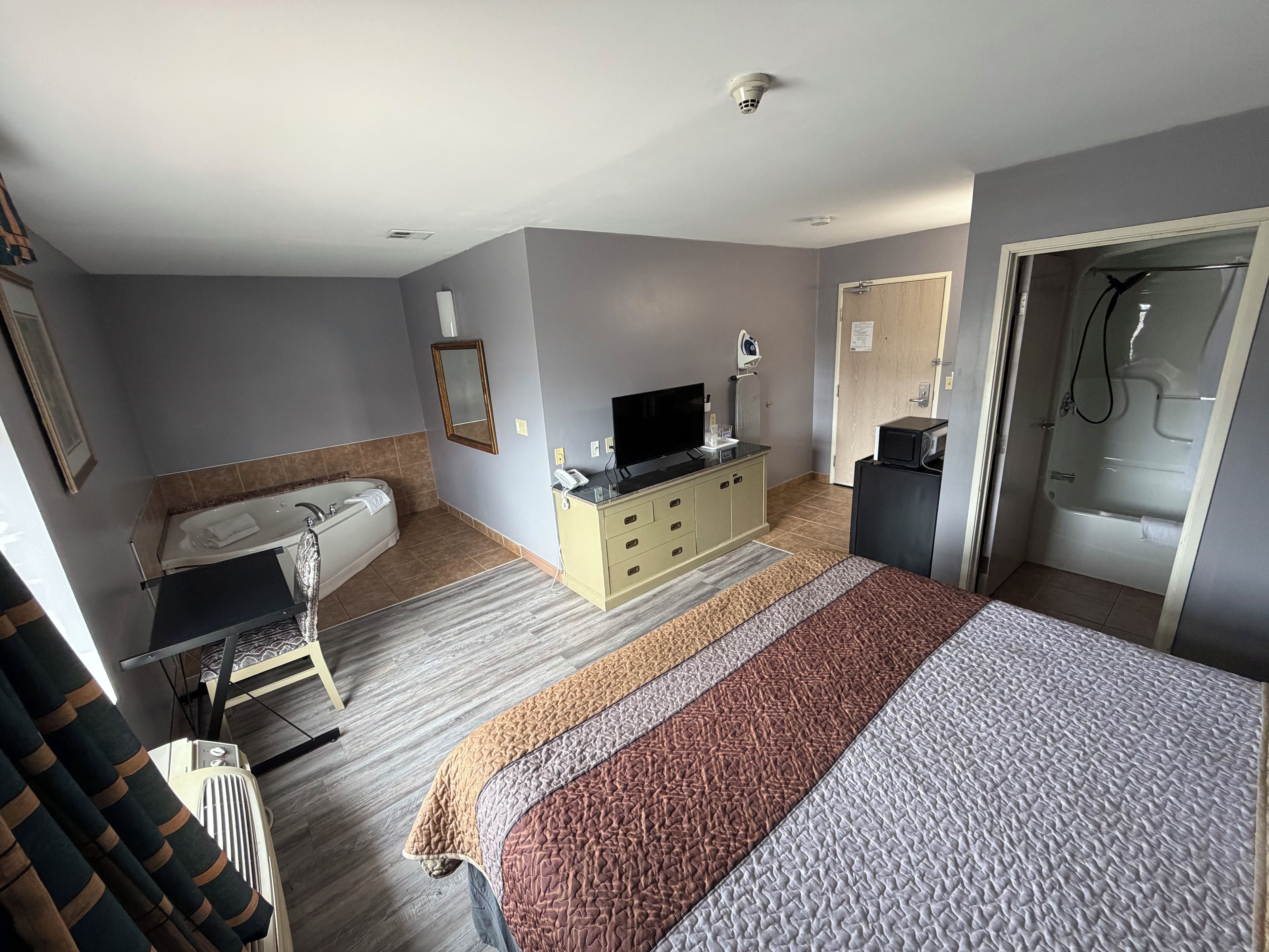 A hotel room with a bed, a television, a bathroom with a bathtub, and a shower.