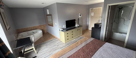 A hotel room with a bed, a television, a bathroom with a bathtub, and a shower.