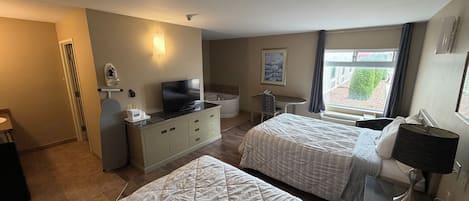 A hotel room with two beds, a desk with a flat-screen TV, a small bathroom, and a window with a view.