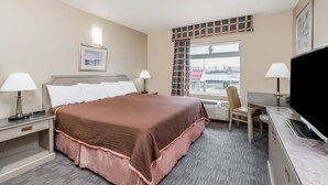 A hotel room with a large bed, two bedside tables with lamps, a desk with a chair, a television, and a window with a view of buildings. - London Travel Inn (London)
