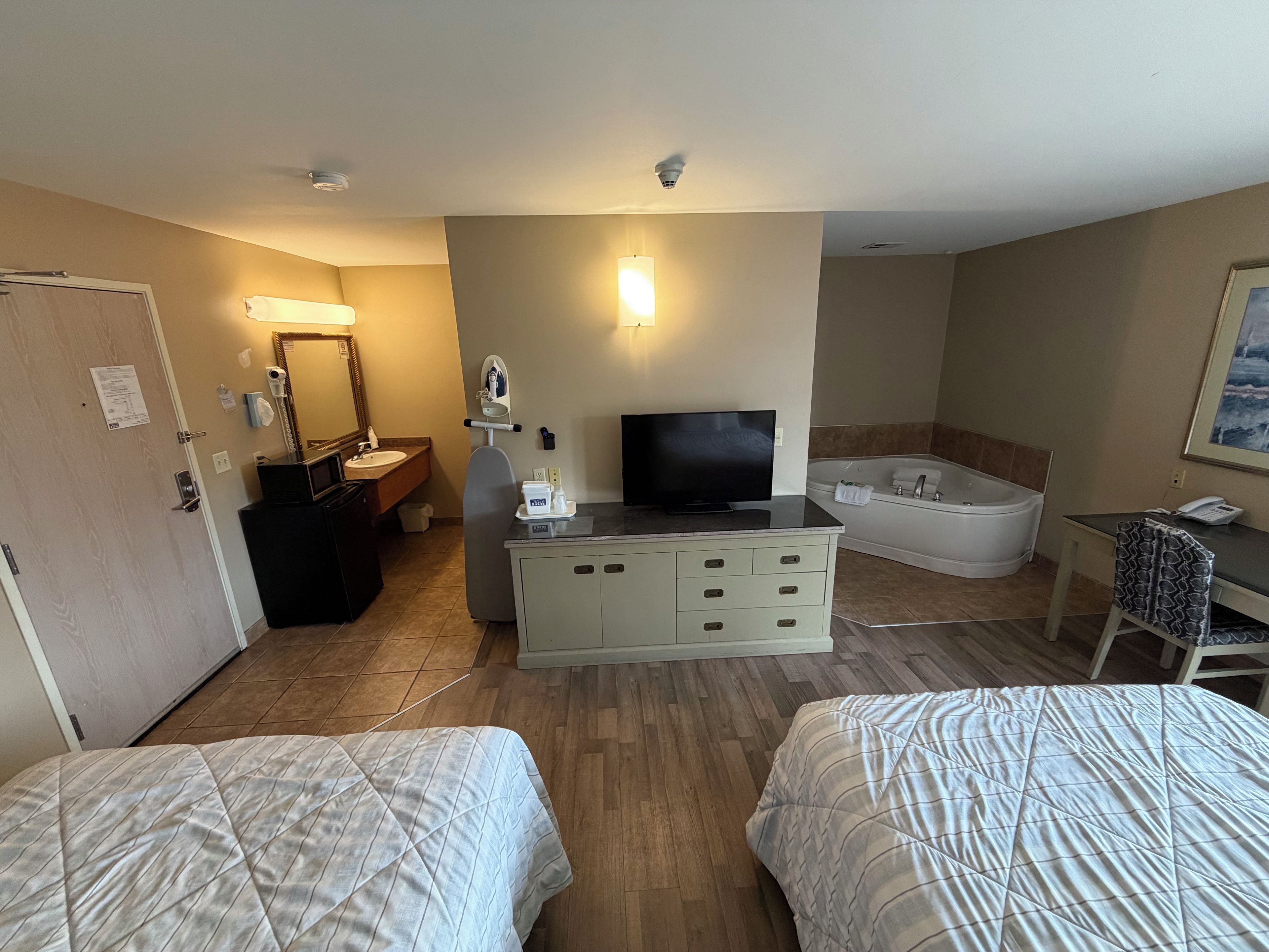 Hotellihuone, jossa on kaksi sänkyä, televisio, kirjoituspöytä puhelimella, kylpyamme ja peili.
