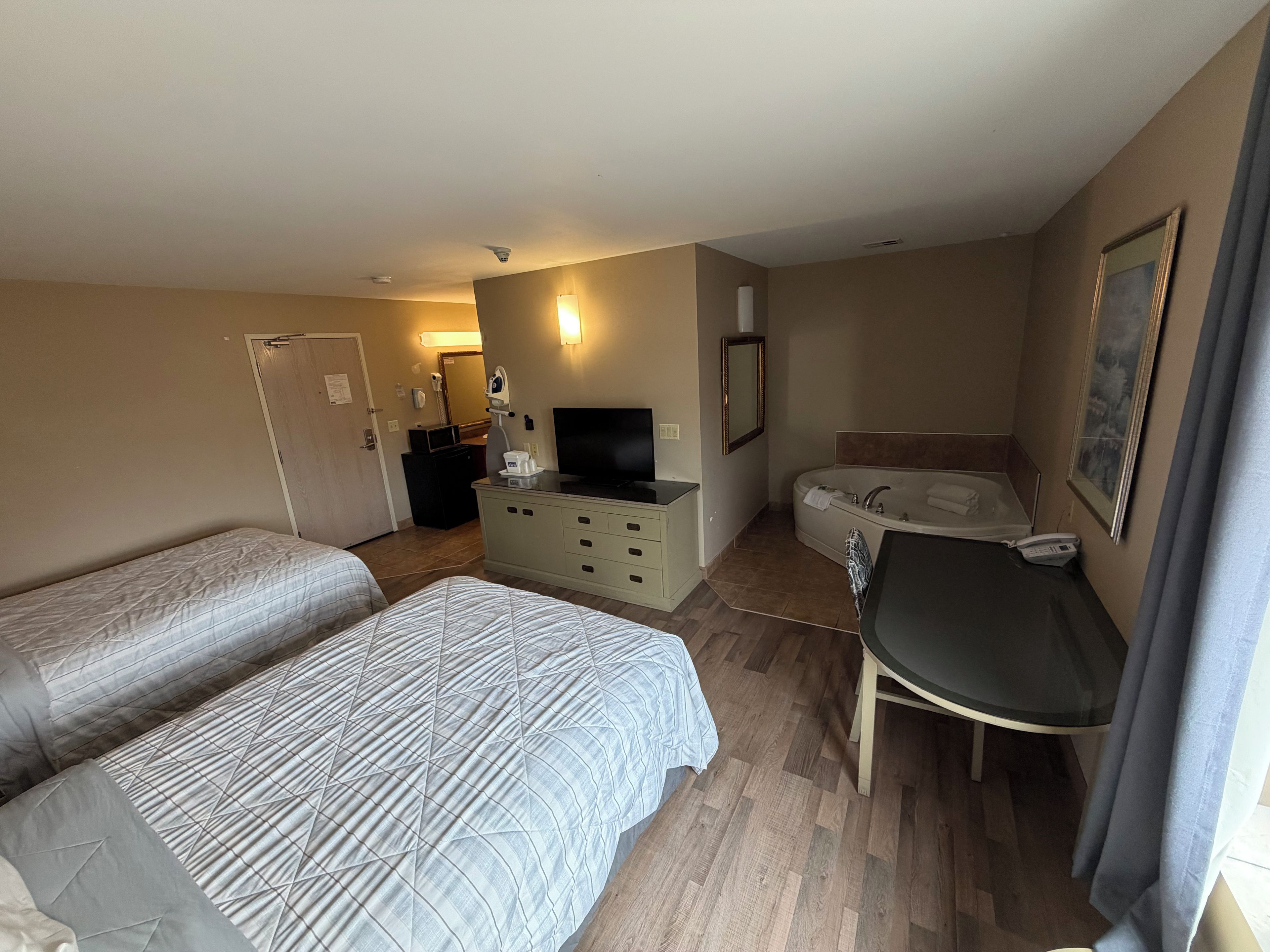 Une chambre d’hôtel avec deux lits, un bureau, une télévision, une salle de bain avec baignoire et un tableau au mur.