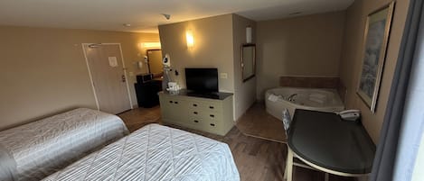 Une chambre d’hôtel avec deux lits, un bureau, une télévision, une salle de bain avec baignoire et un tableau au mur.