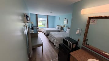 A hotel room with two beds, a desk, a microwave, a sink, and a mirror.