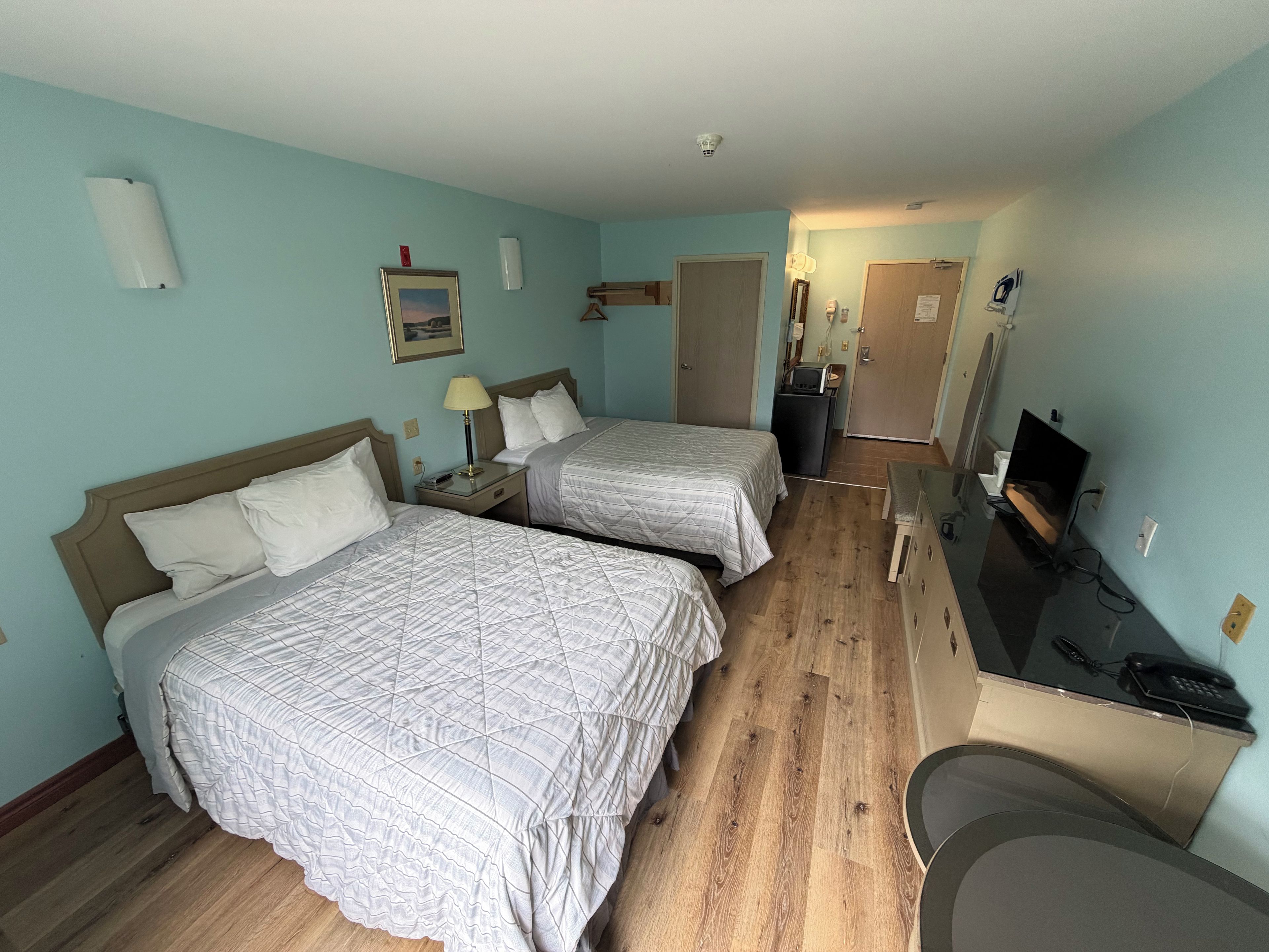 A hotel room with two beds, a desk with a computer, a TV, and a small kitchenette.