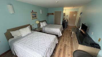 Een hotelkamer met twee bedden, een bureau met een computer, een televisie en een kleine kitchenette.