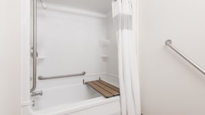 A white bathtub with a wooden shelf, grab bars, and a shower curtain. - London Travel Inn (London)