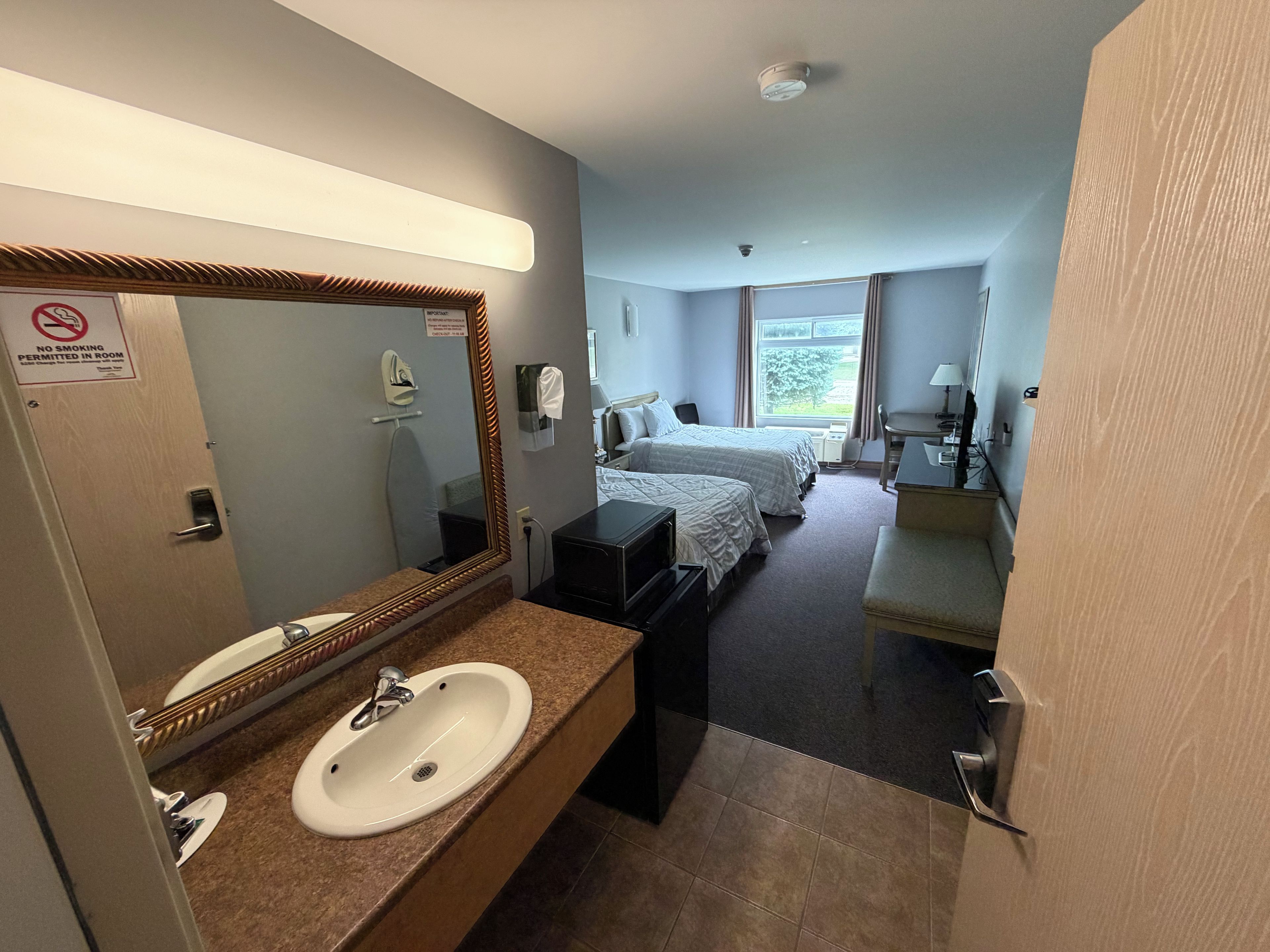 A hotel room with a bathroom, a bed, a desk, and a window.
