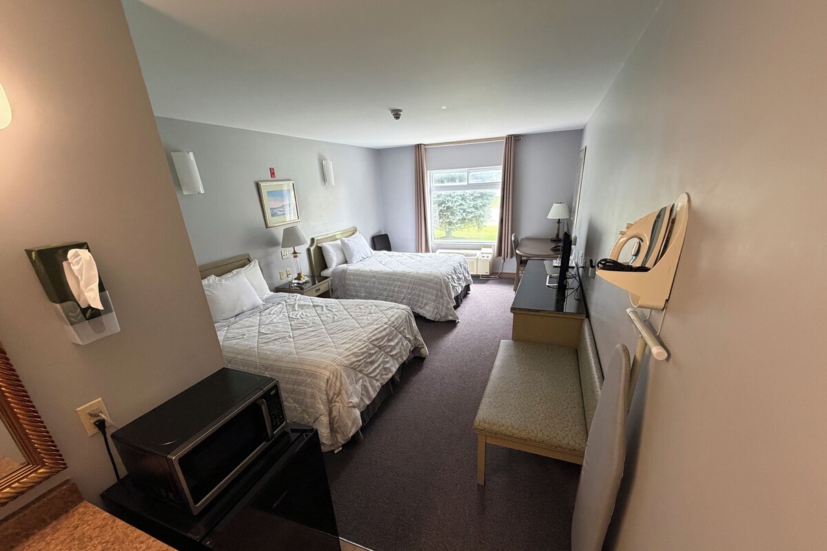 A hotel room with two beds, a desk, a chair, a TV, and a bathroom area.
