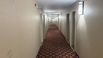 A hotel hallway with patterned carpet, doors, and wall-mounted light fixtures.