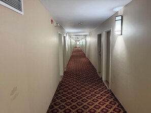 A hotel hallway with patterned carpet, doors, and wall-mounted light fixtures. - London Travel Inn (London)