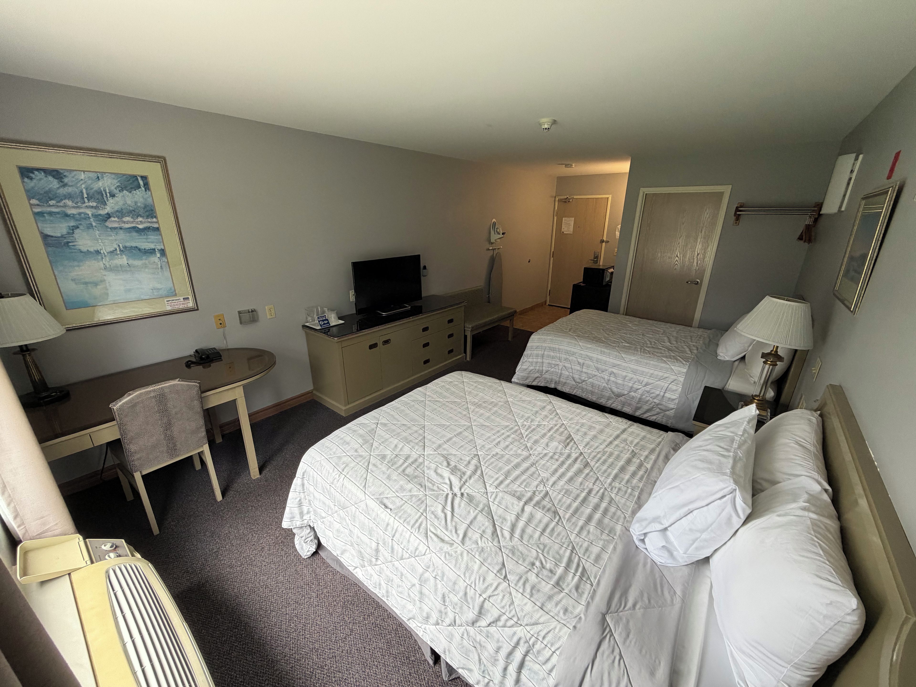 A hotel room with a bed, two bedside tables, a desk, a chair, a television, and a painting on the wall.