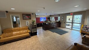 A lobby with a reception desk, a leather sofa, a small refrigerator, and a tiled floor.