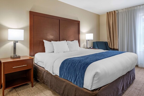 A hotel room with a large bed, two bedside tables, a nightstand, a chair, and a window with curtains. - Comfort Inn & Suites Northern Kentucky (Newport)