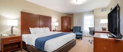 Habitación de hotel con una cama grande, un escritorio con ordenador, una silla y un televisor.