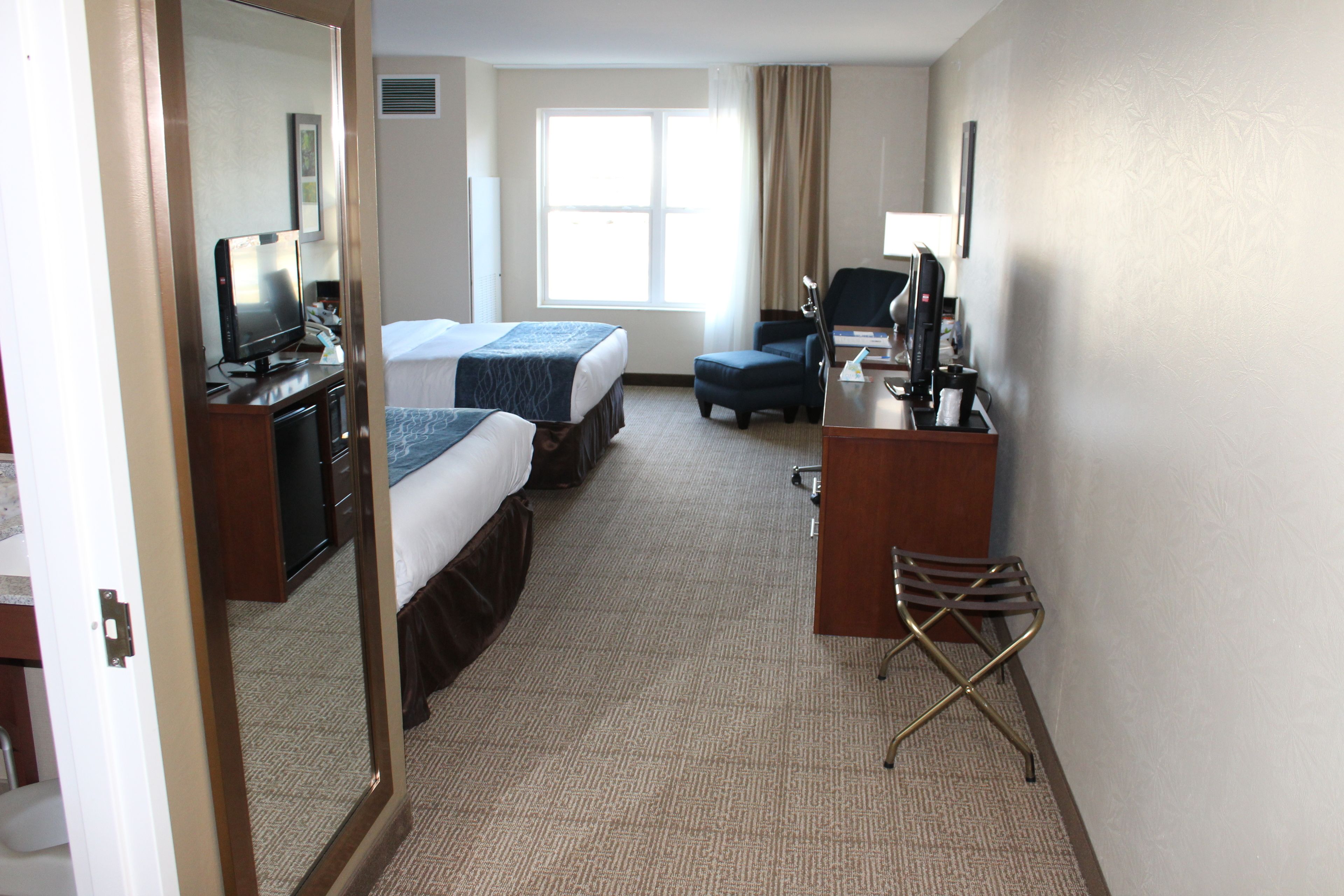 A hotel room with two beds, a desk with a computer, a chair, and a mirror.