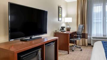 A hotel room with a flat-screen TV, a desk with a chair, a mini-fridge, a microwave, a telephone, and a bed.